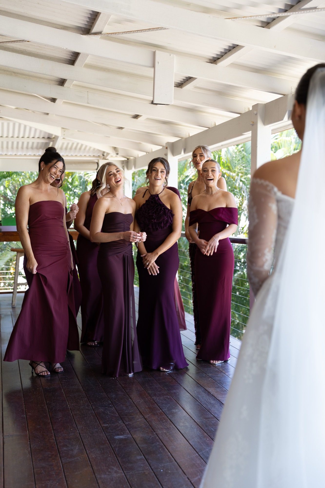 Bridesmaids in burgundy seeing the bride for the first time on the timber verandah, Airlie Beach