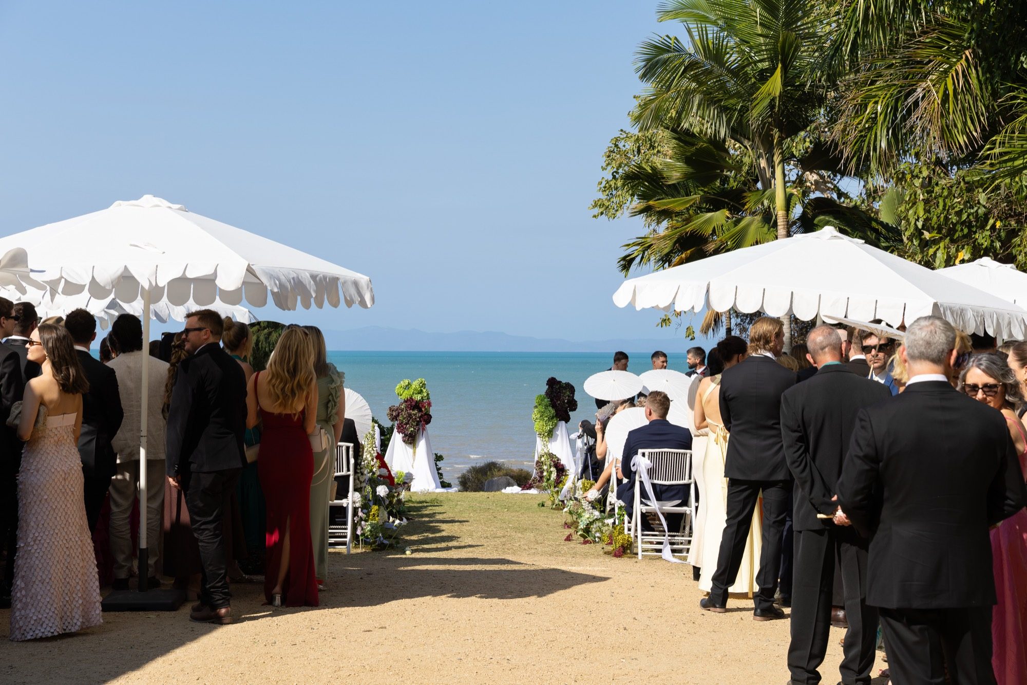 Ceremony aisle looking out to the Coral Sea, white scalloped umbrellas and guests, Freedom Shores, Airlie Beach