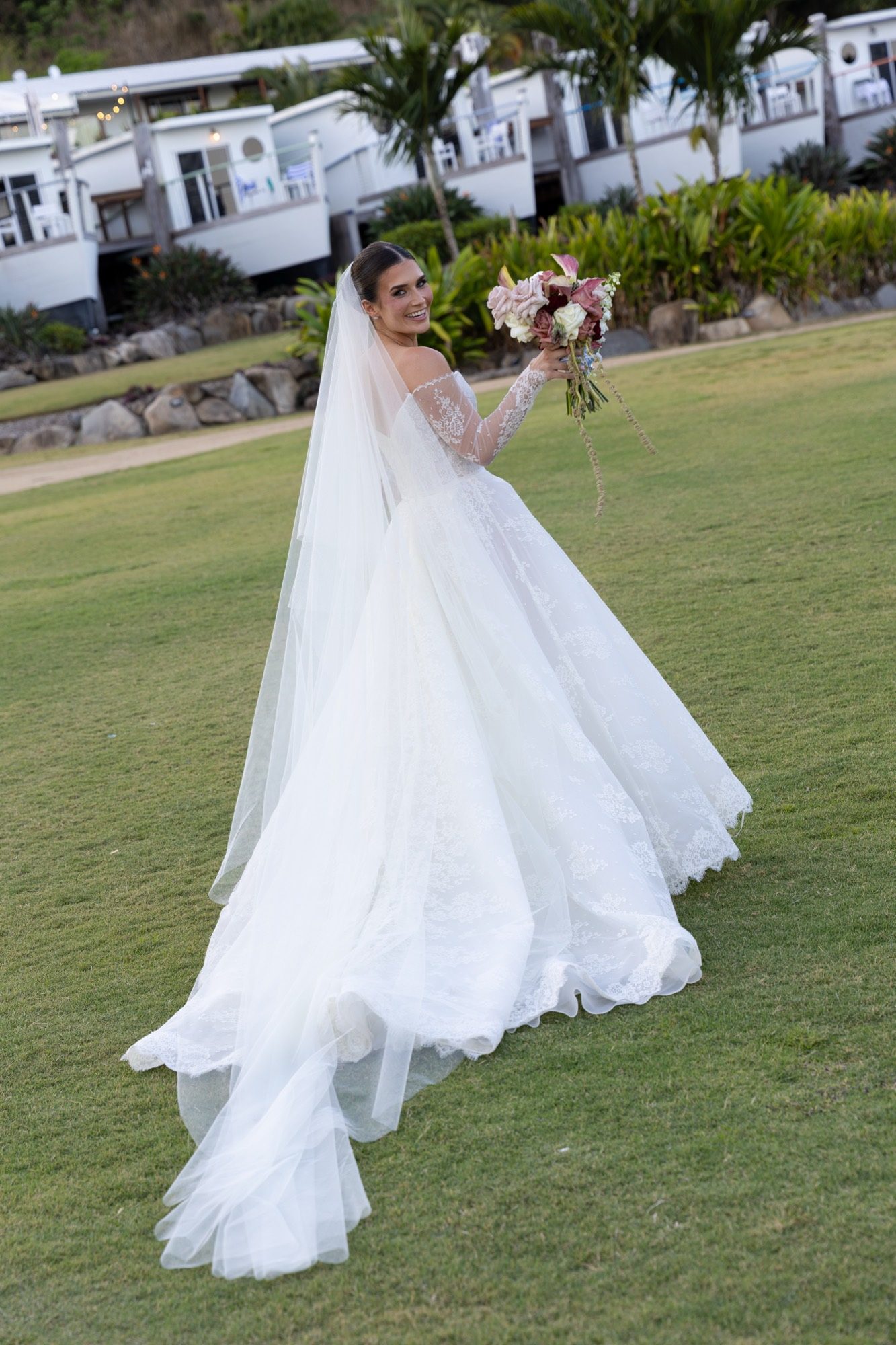 The bride looking back over her shoulder on the lawn, veil trailing, Freedom Shores, Airlie Beach