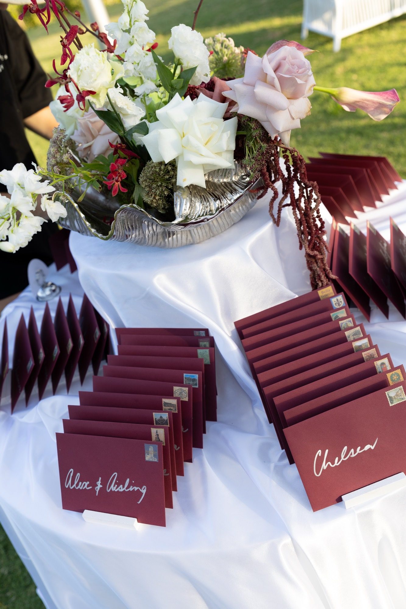 Burgundy place cards with vintage stamps and a silver shell bowl of roses on the escort table, Airlie Beach